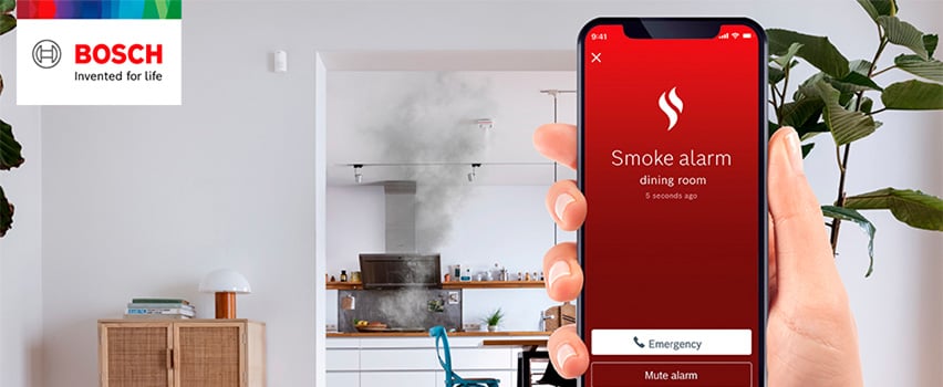 Bosch Smart Home-app viser røykvarsler-varsling fra spisestue med nødanrop-knapp og røyk fra kjøkken i bakgrunnen