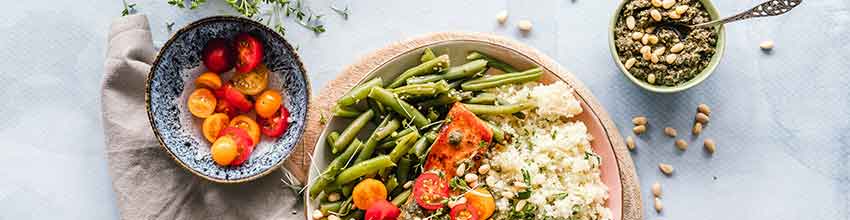 På et bord står en laksebowl med blomkålsris og grønne bønner, toppet med tomater og pesto.