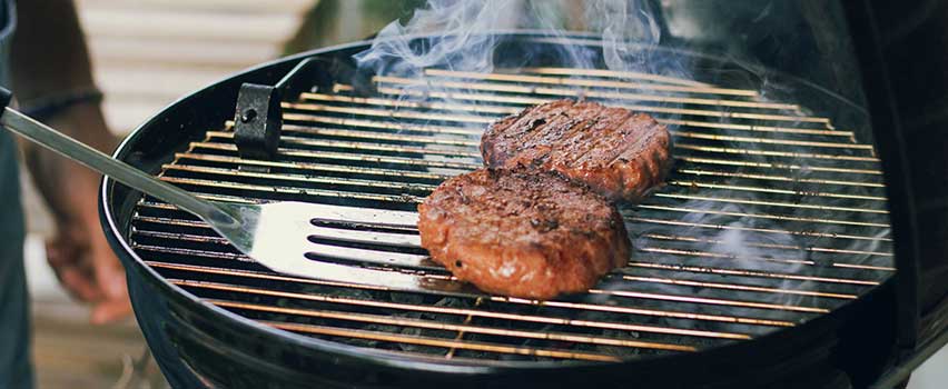 Biffer stekes over glødende kull på klassisk kullgrill med grillredskap i bruk.