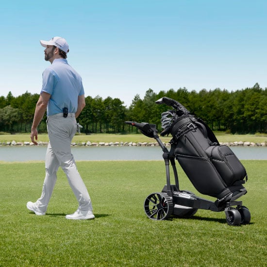 Golfspiller går ved siden av Navee elektrisk golftralle med golfbag på golfbanen