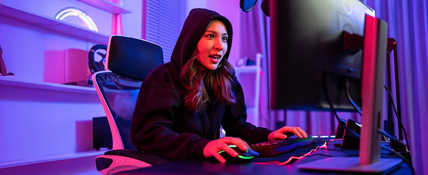Ung kvinne gamer ved datamaskinen med Wozinsky gaming-mus og tastatur i mørkt rom med lilla RGB-belysning