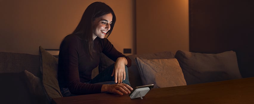 Kvinne smiler mens hun lader smarttelefonen trådløst med Wozinsky powerbank på bordet i koselig kveldsbelysning