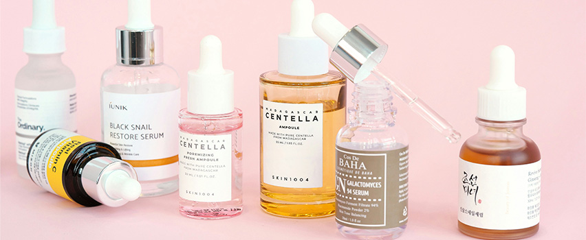 Hudpleieprodukter står oppstilt på rekke med rosa bakgrunn.