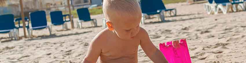 Baby på sommerstrand leker med strandleketøy.